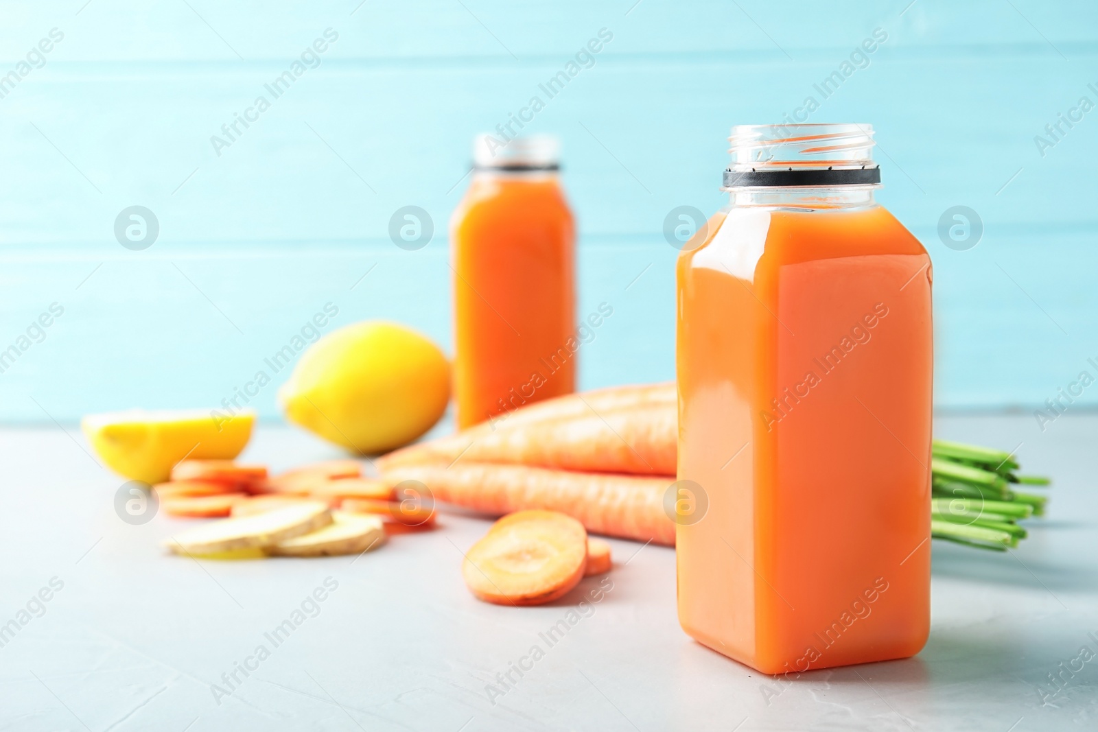 Photo of Bottles with carrot juice and fresh ingredients on table