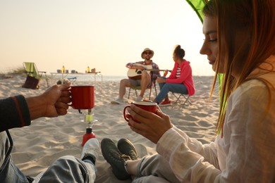 Photo of Friends resting on sandy beach. View from camping tent