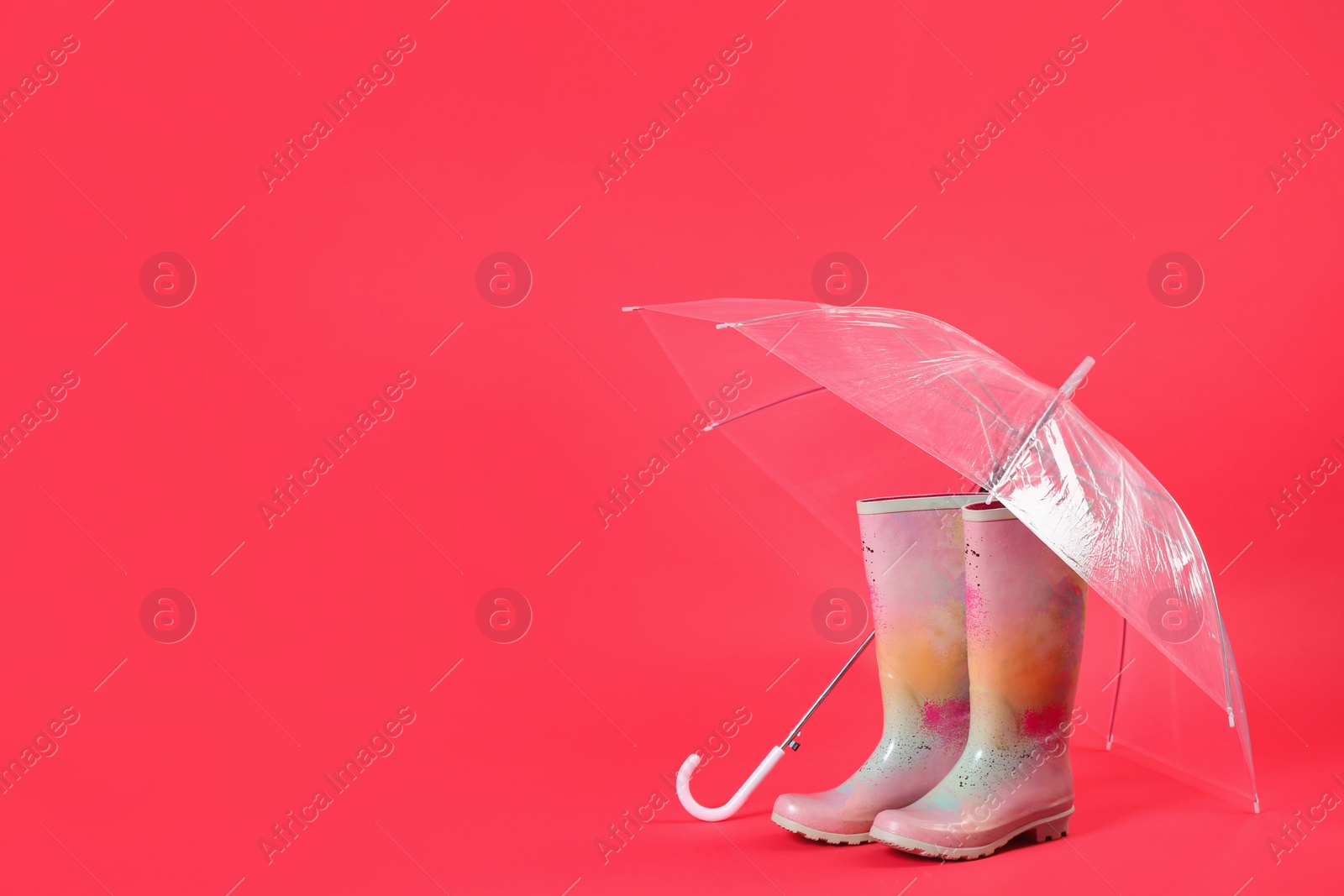 Photo of Transparent umbrella and colorful rubber boots on red background. Space for text