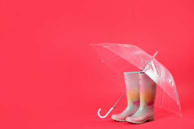 Photo of Transparent umbrella and colorful rubber boots on red background. Space for text