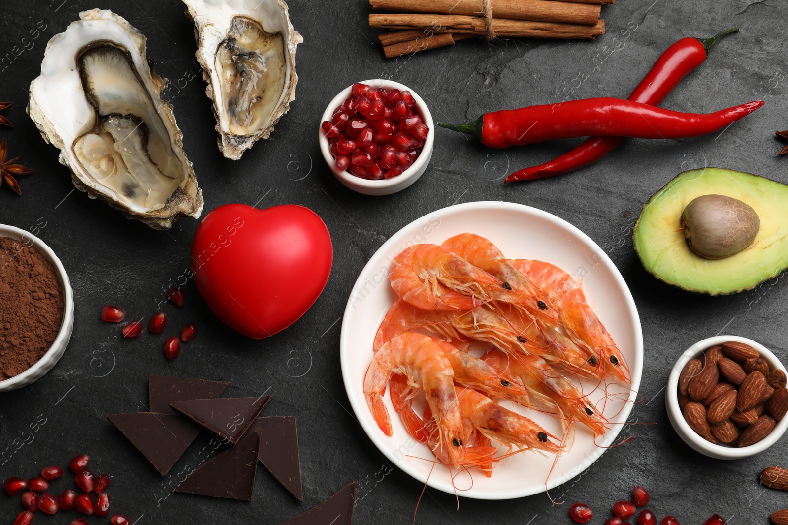 Photo of Natural aphrodisiac. Different food products and heart model on black table, flat lay