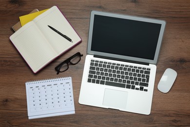 Photo of Modern laptop, glasses and office stationery on wooden table, flat lay. Distance learning