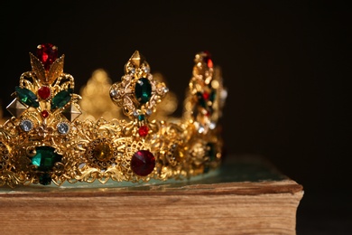 Photo of Beautiful golden crown on old book against black background, closeup. Fantasy item