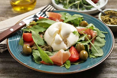 Photo of Delicious burrata salad served on wooden table, closeup