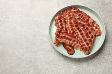 Photo of Plate with fried bacon slices on grey textured table, top view. Space for text