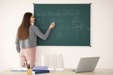 Young female teacher writing on blackboard in classroom