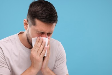Photo of Allergy symptom. Man sneezing on light blue background. Space for text