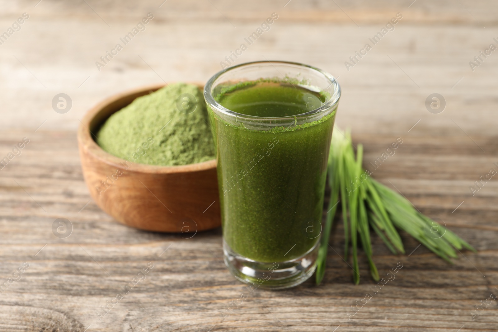 Photo of Wheat grass drink in shot glass on wooden table, closeup