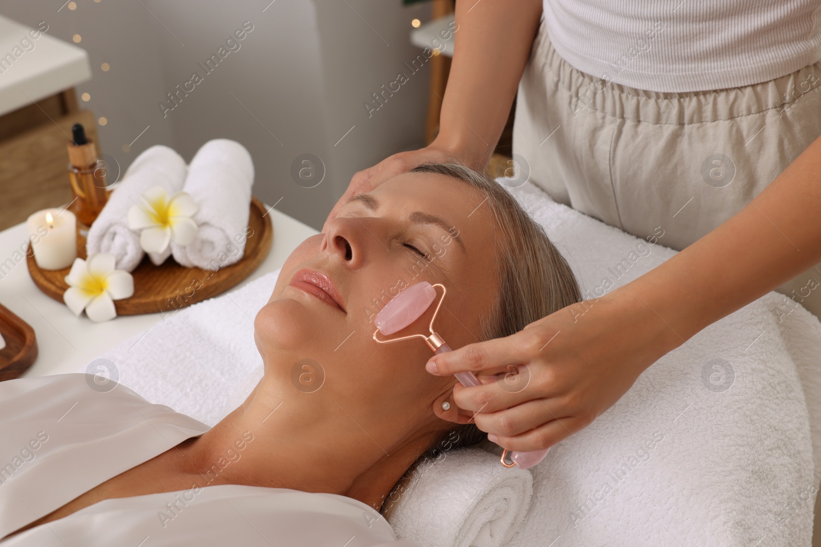 Photo of Woman receiving facial massage with rose quartz roller in beauty salon, closeup