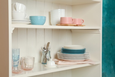 Photo of White shelving unit with set of dishware near wall