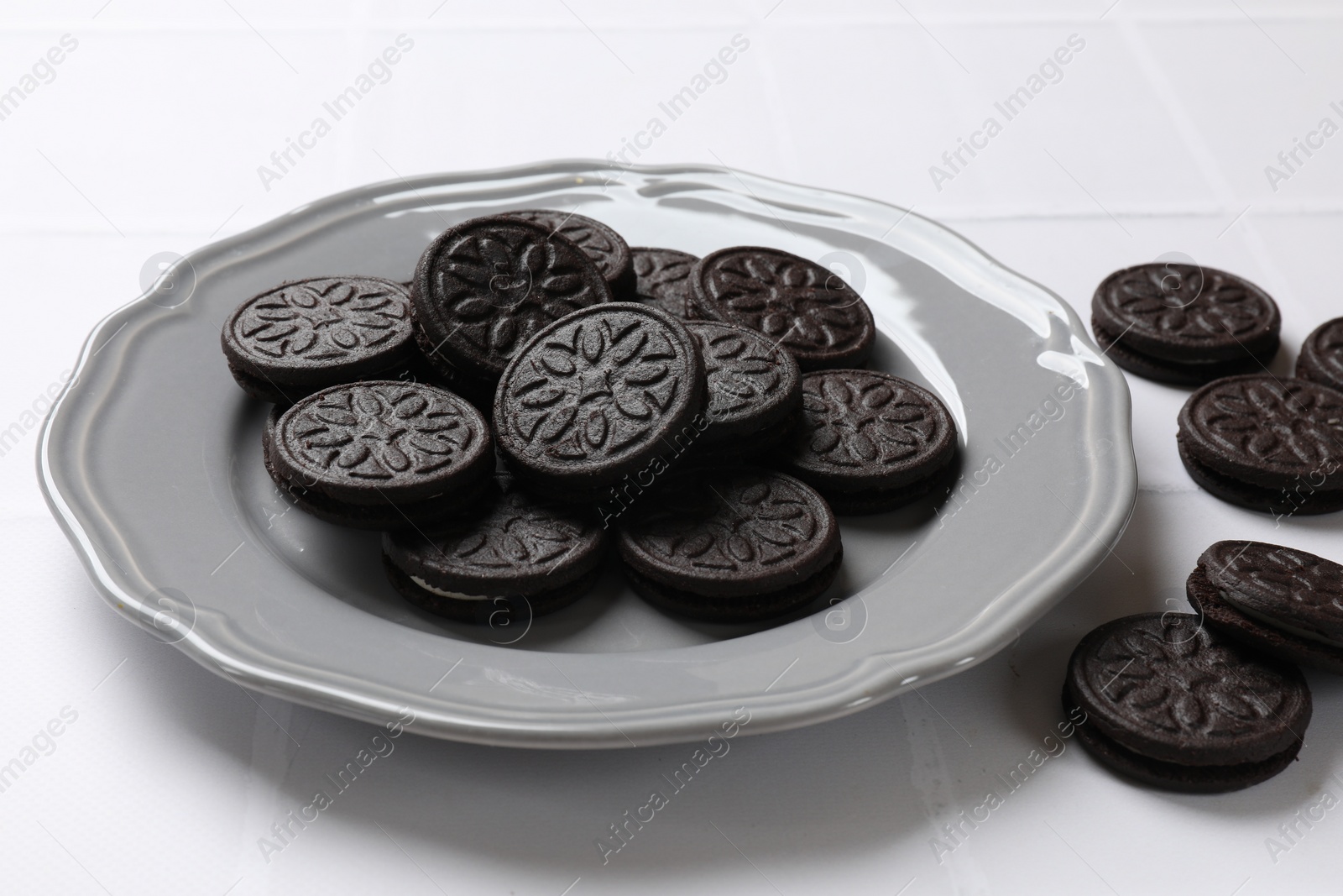 Photo of Plate with tasty sandwich cookies on white tiled table, closeup