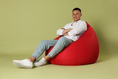 Photo of Handsome man with crossed arms on red bean bag chair against green background