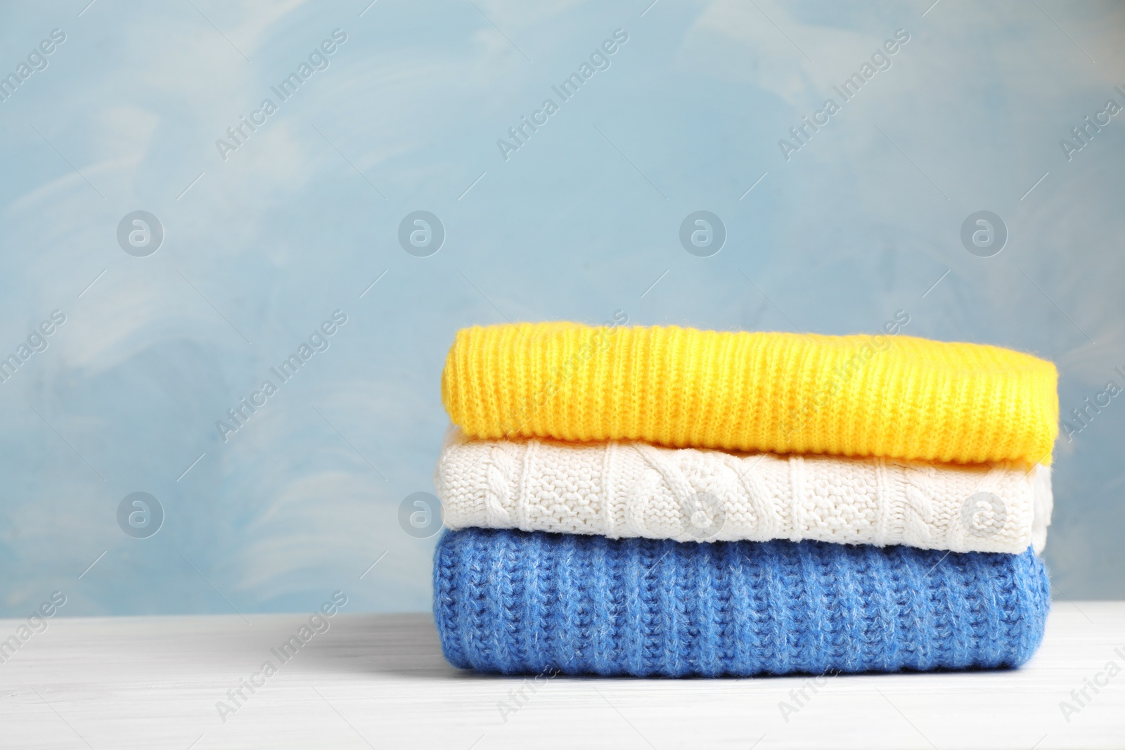 Photo of Stack of folded knitted sweaters on table. Space for text