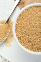 Photo of Brown sugar in bowl and spoon on white table, flat lay