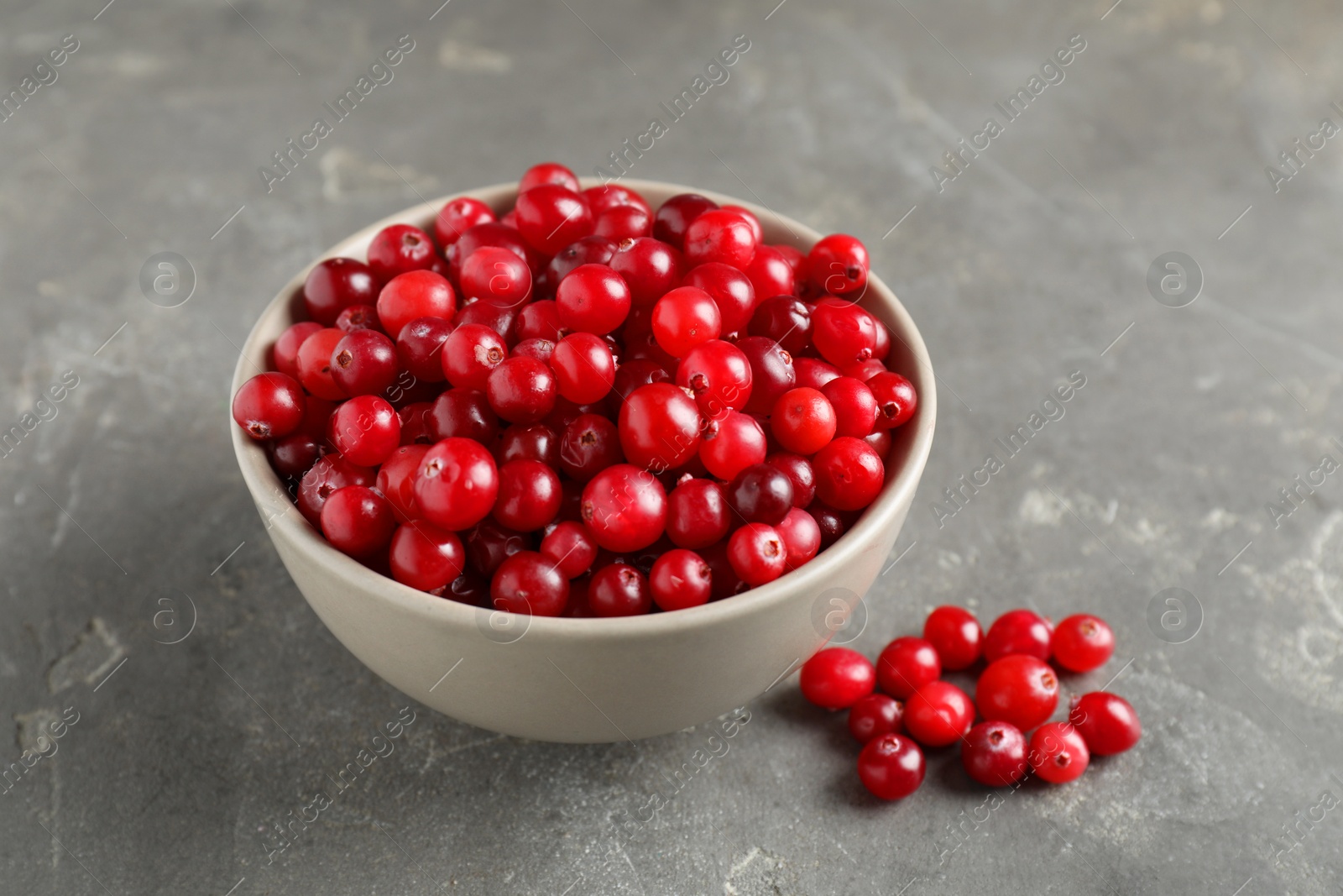 Photo of Cranberries in bowl on light grey table, closeup