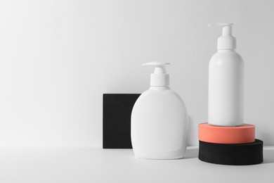Photo of Bottles with different cosmetic products and podiums on white background, space for text