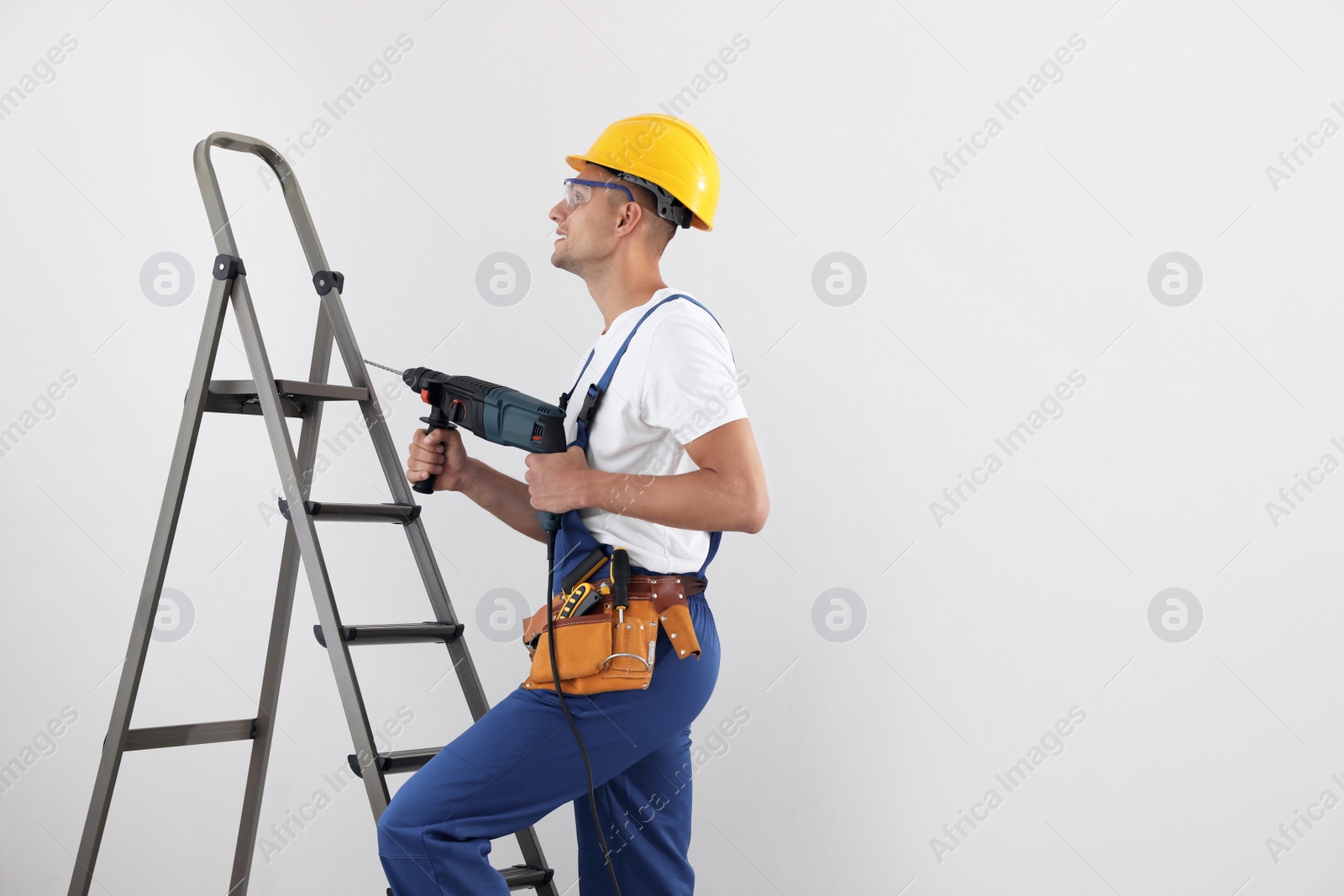 Photo of Worker with electric drill on ladder indoors, space for text