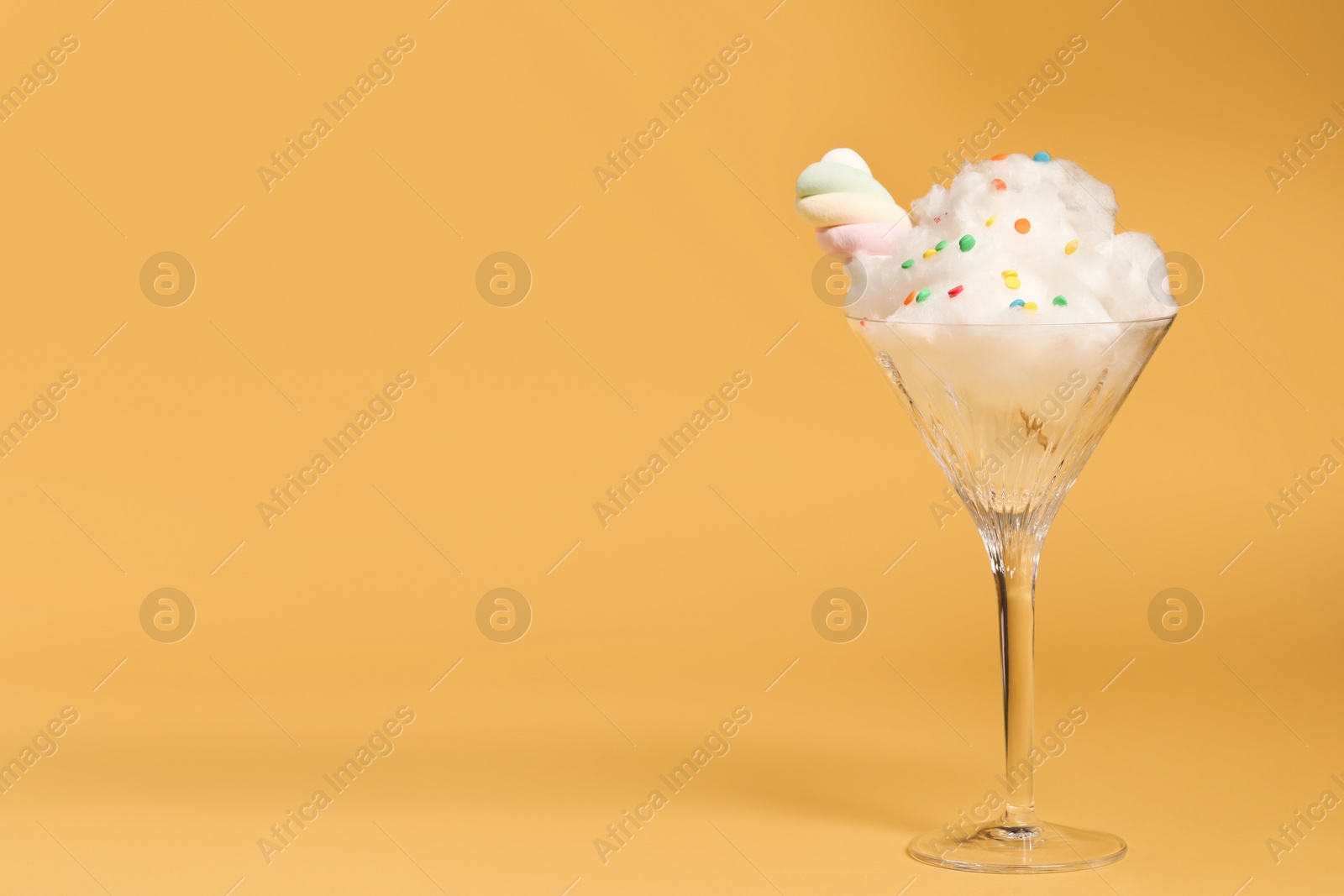 Photo of Martini glass with cotton, sprinkles and marshmallow on yellow background. Space for text