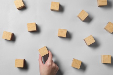 Photo of Woman arranging wooden cubes at light grey table, top view