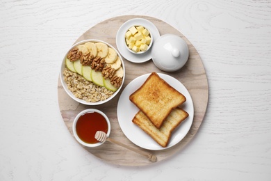 Photo of Tasty breakfast with oatmeal porridge and toasts served on white wooden table, top view