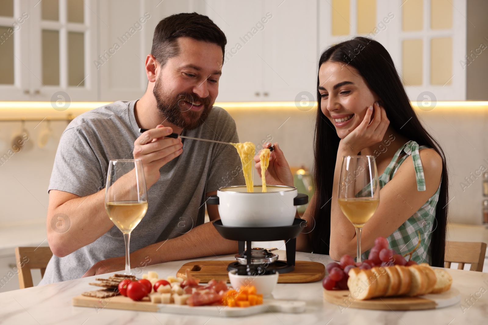 Photo of Affectionate couple enjoying cheese fondue during romantic date in kitchen