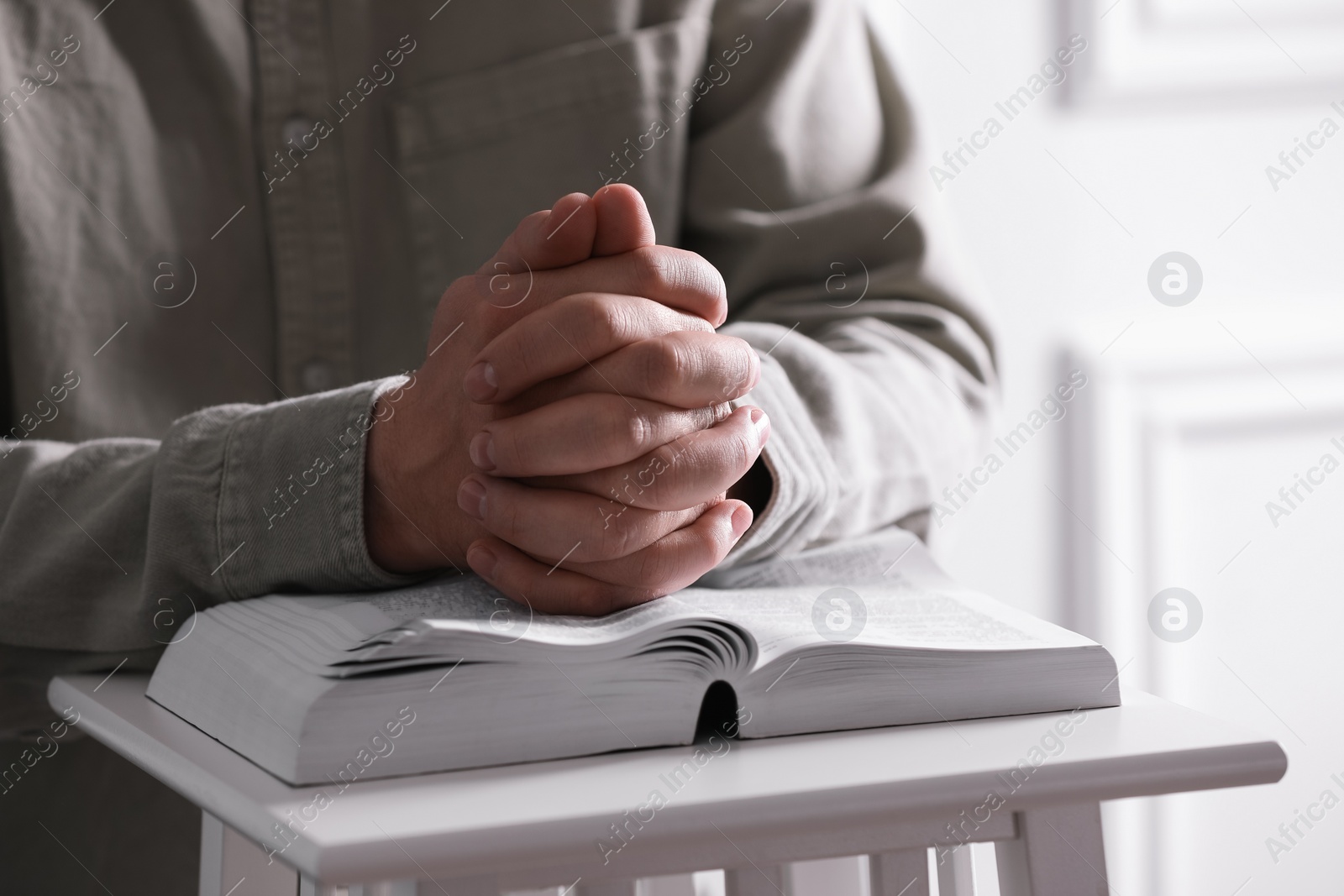 Photo of Religion. Christian man praying over Bible indoors, closeup