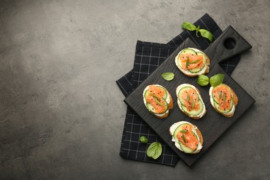 Tasty canapes with salmon, cucumber and cream cheese on grey table, top view. Space for text