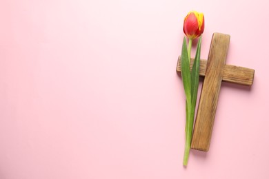 Easter - celebration of Jesus resurrection. Wooden cross and tulip on pink background, top view. Space for text