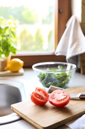 Photo of Cut fresh tomato and knife near sink in kitchen, space for text