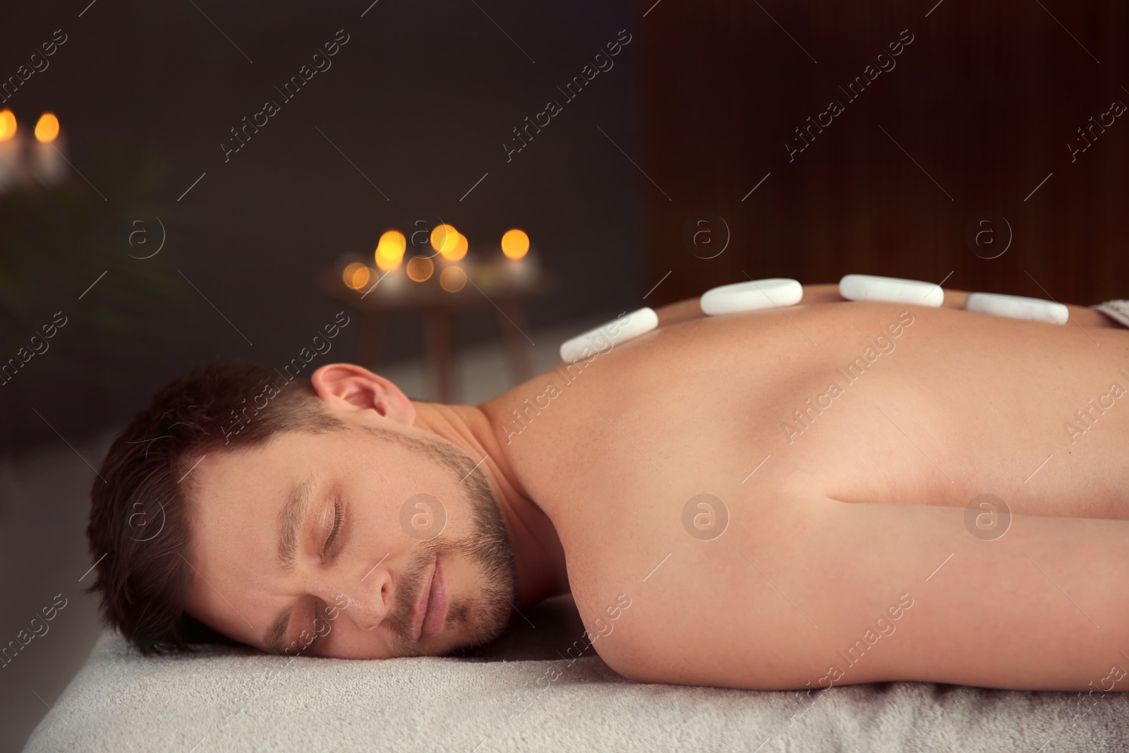 Photo of Handsome man receiving hot stone massage in spa salon