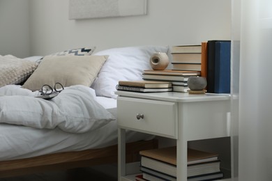 Photo of Hardcover books and scented candles on white bedside table in bedroom