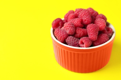 Photo of Bowl of delicious ripe raspberries on yellow background. Space for text