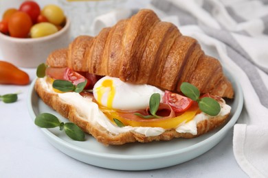 Tasty croissant with fried egg, tomato and microgreens on white table, closeup