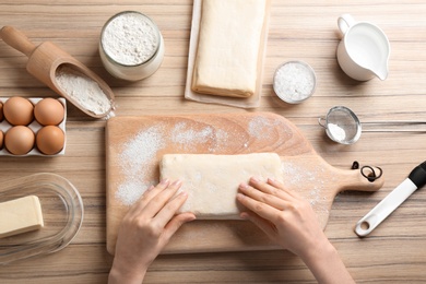 Young woman with puff pastry dough and ingredients on wooden table, top view