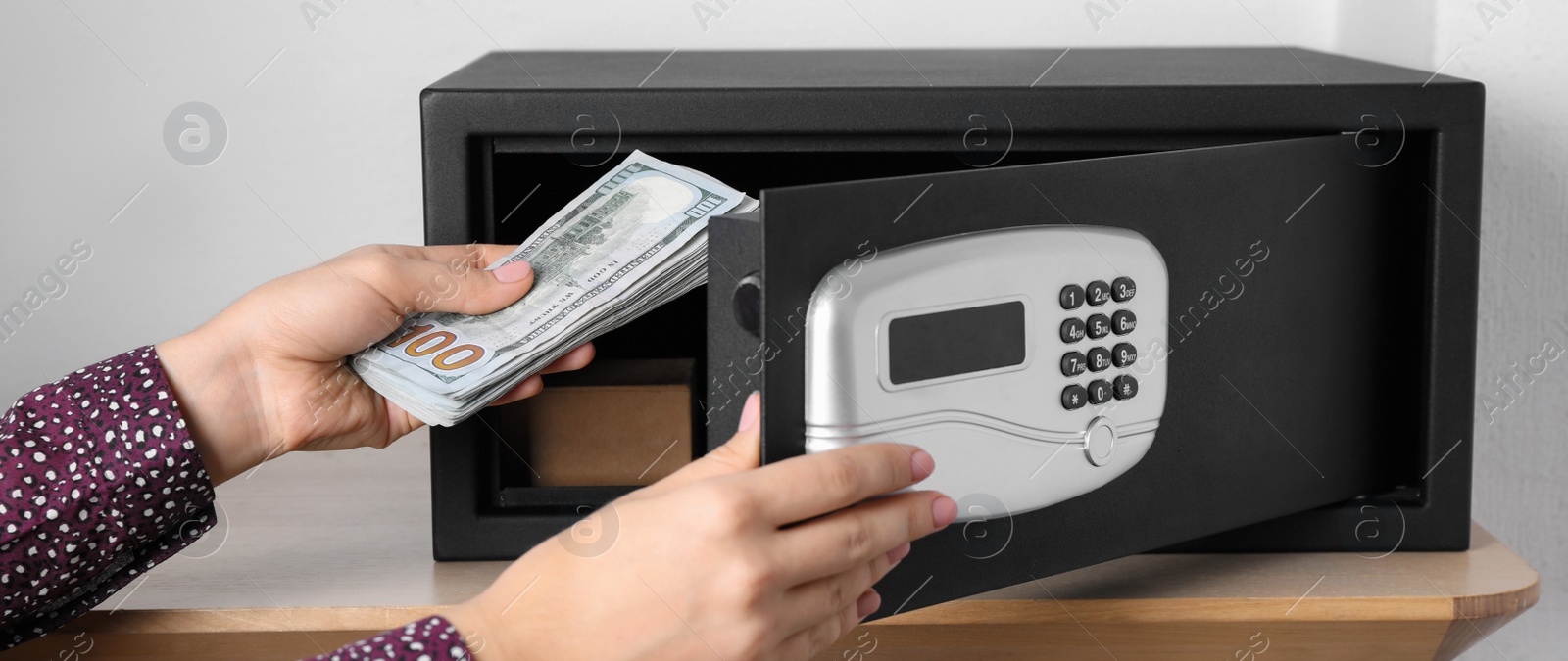 Image of Woman putting money into steel safe with electronic lock, closeup. Banner design