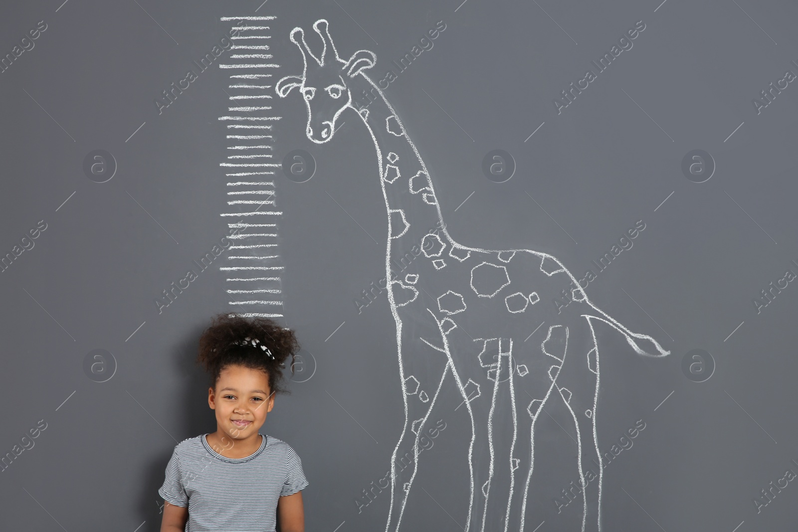 Photo of African-American child measuring height near chalk giraffe drawing on grey background