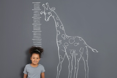 African-American child measuring height near chalk giraffe drawing on grey background