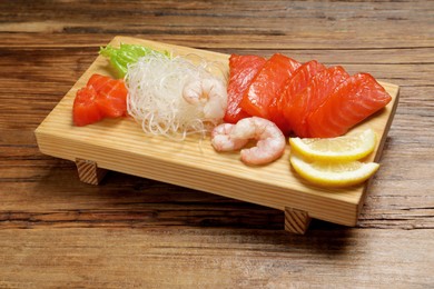 Photo of Delicious sashimi set of salmon and shrimps served with funchosa and lemon on wooden table