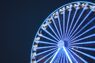 Photo of Big glowing Ferris wheel against dark blue sky at night. Space for text