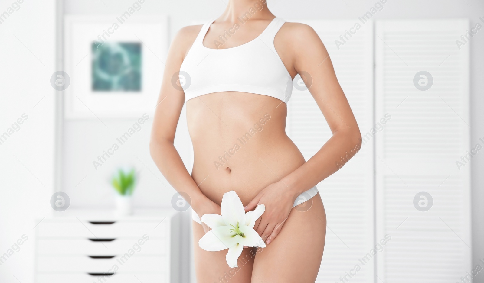 Photo of Young woman with flower showing smooth skin after bikini epilation indoors