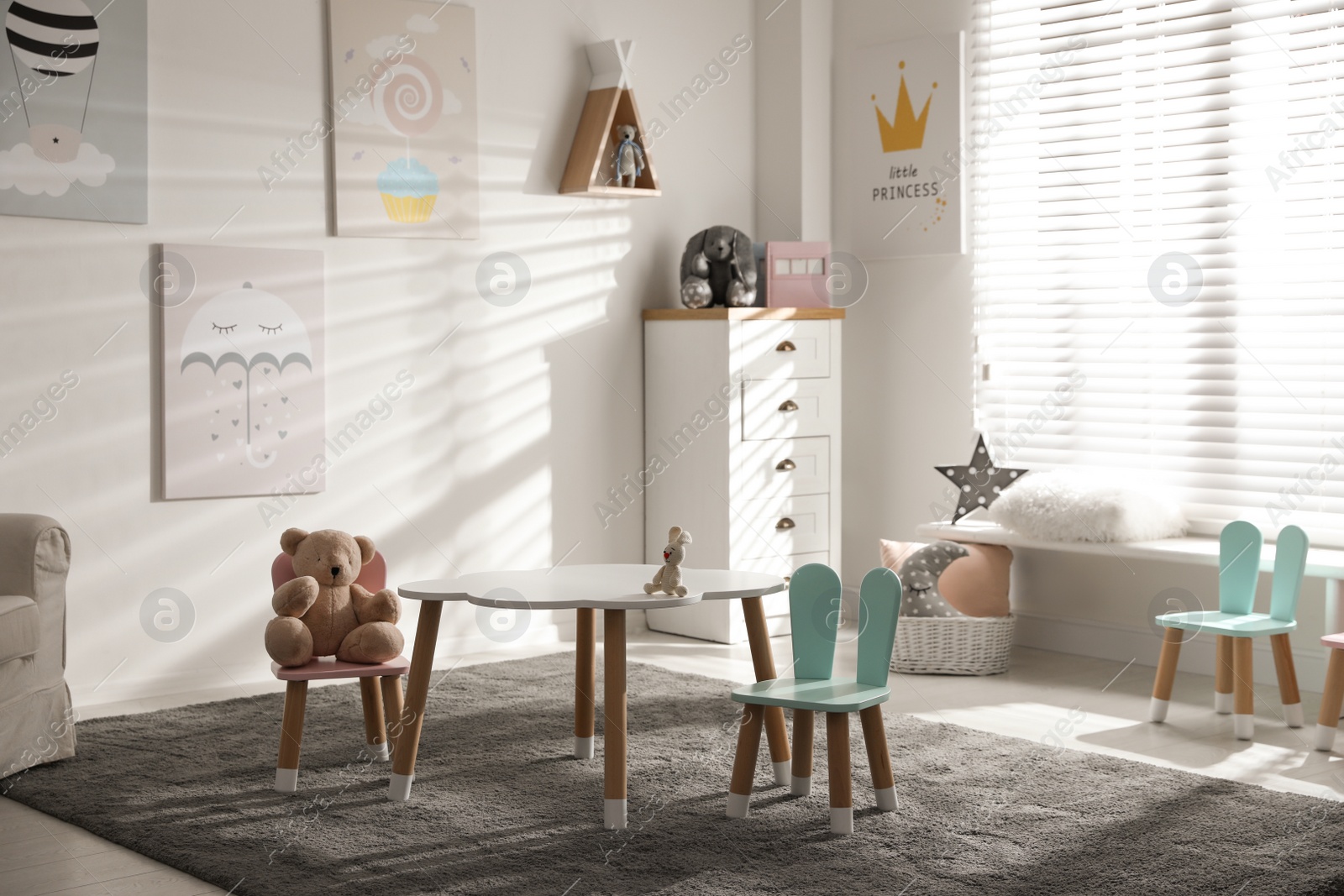 Photo of Small table and chairs with bunny ears in children's room interior