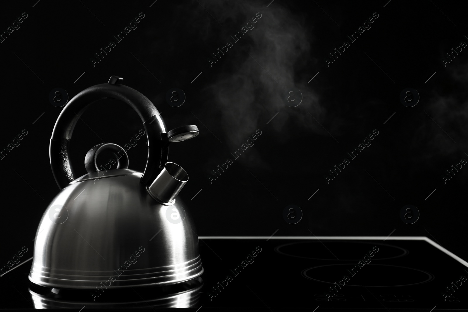 Photo of Modern kettle with whistle on stove against black background, space for text