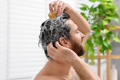 Photo of Man washing his hair with solid shampoo bar in bathroom, closeup