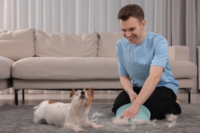 Photo of Smiling man with brush and pan removing pet hair from carpet at home