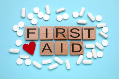 Words First Aid made of wooden cubes, pills and cardboard heart on light blue background, flat lay