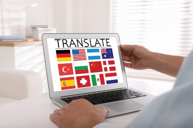 Translator using modern laptop with images of different flags on screen at white table indoors, closeup