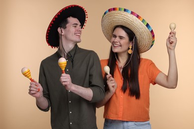 Photo of Lovely couple woman in Mexican sombrero hats with maracas on beige background