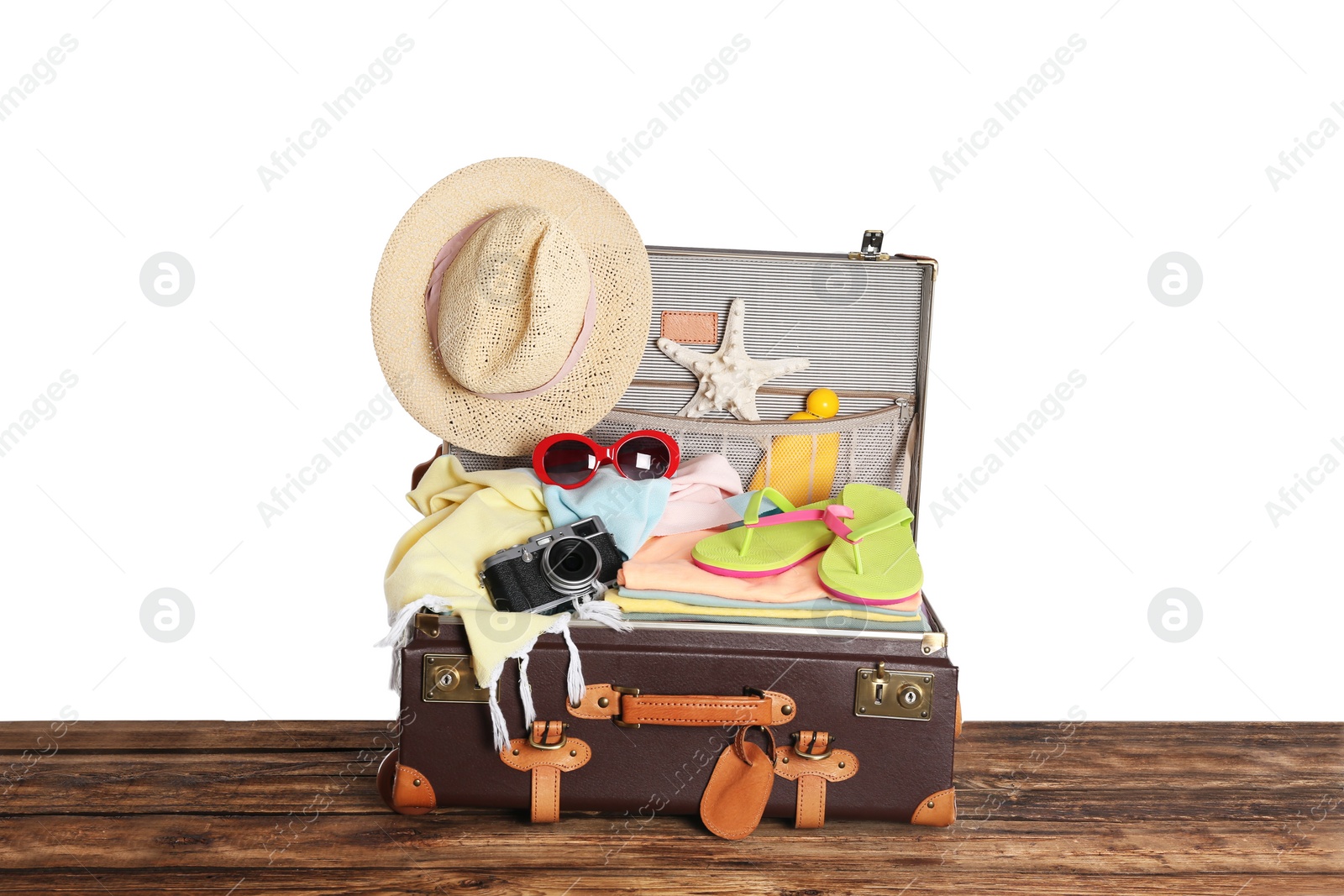 Photo of Open vintage suitcase with different beach objects packed for summer vacation on wooden table against white background