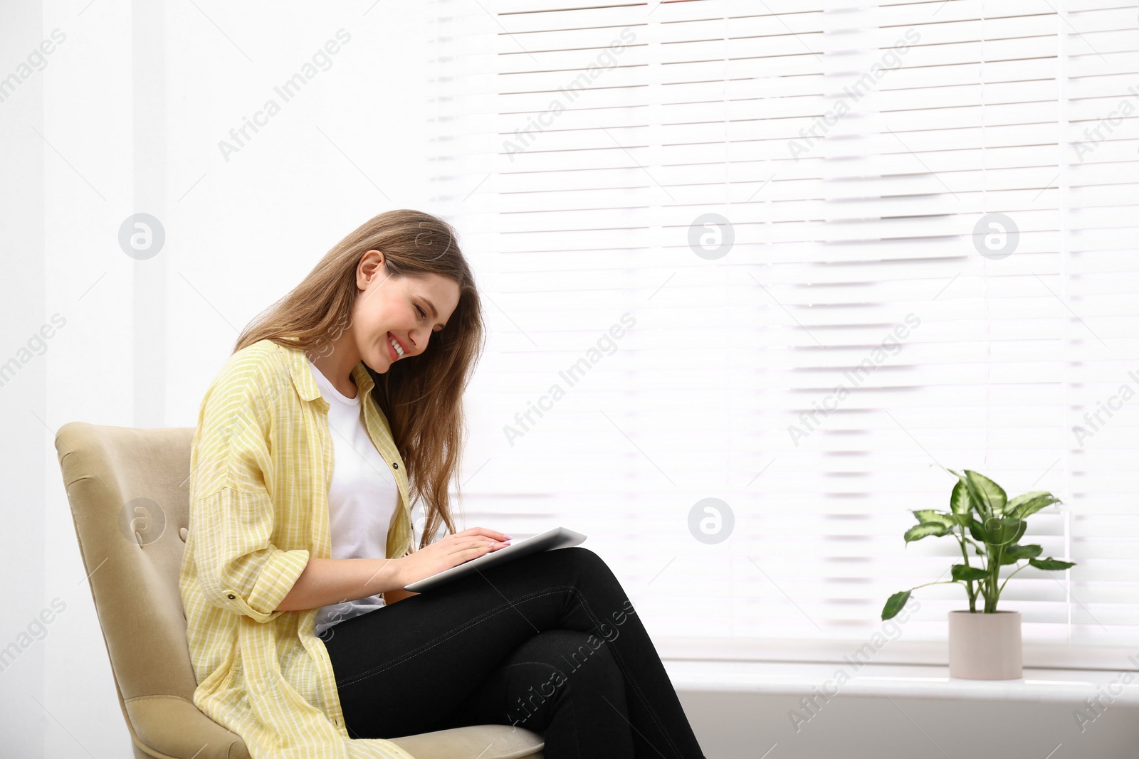Photo of Young woman with tablet resting in armchair at home. Space for text