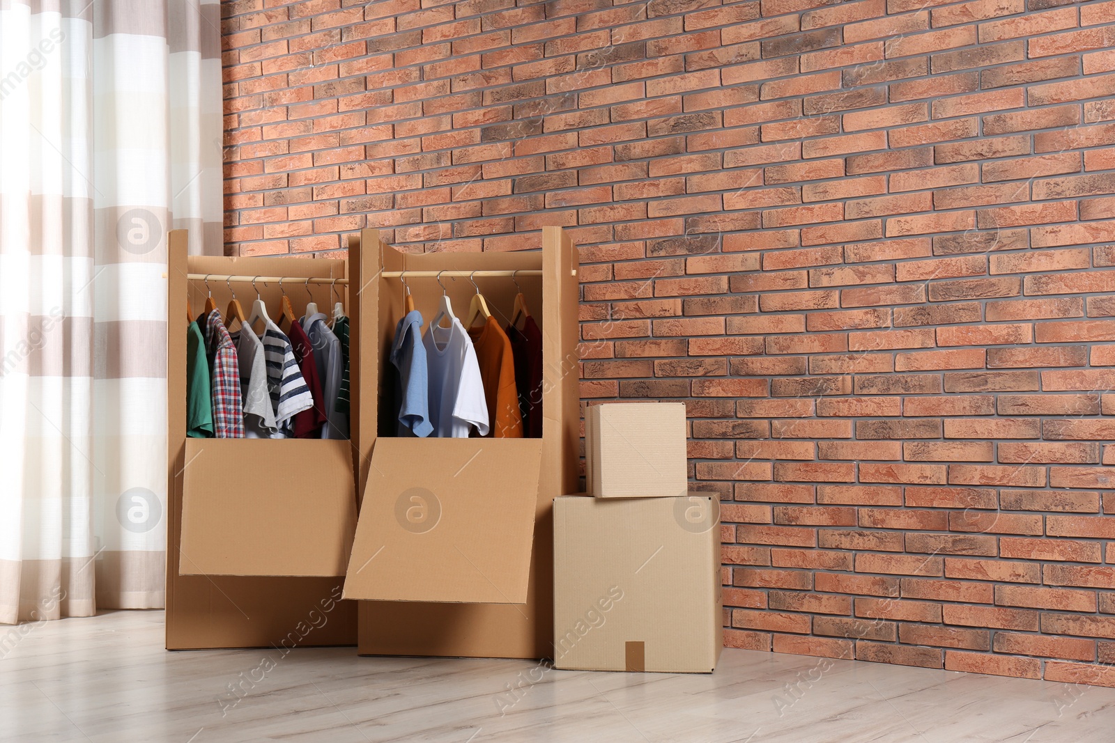 Photo of Wardrobe boxes with clothes against brick wall indoors. Space for text